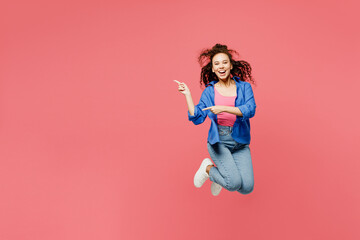 Full body young woman of African American ethnicity she wears blue shirt casual clothes jump high point index finger aside on area isolated on plain pastel pink background studio. Lifestyle concept.