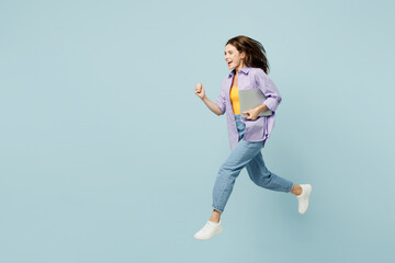 Fototapeta na wymiar Full body side view young happy IT woman she wears purple shirt yellow t-shirt casual clothes jump high hold closed laptop pc computer run fast isolated on plain pastel light blue background studio .