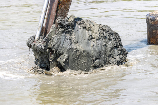 Dredging the bottom of water area, view of the bucket of the floating excavator full of mud