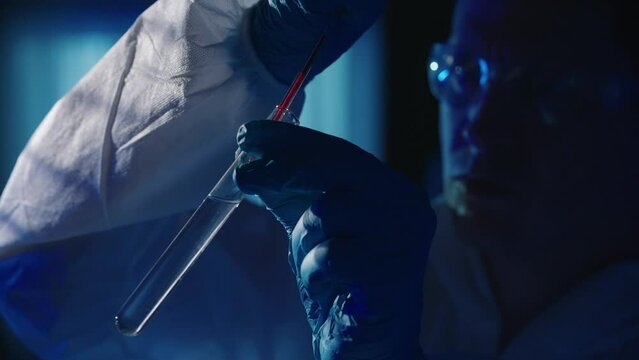 A forensic investigator adds a blood sample to a test tube with a reagent using a pipette. A man collects evidence at the crime scene, in a dark apartment lit by red and blue police sirens.