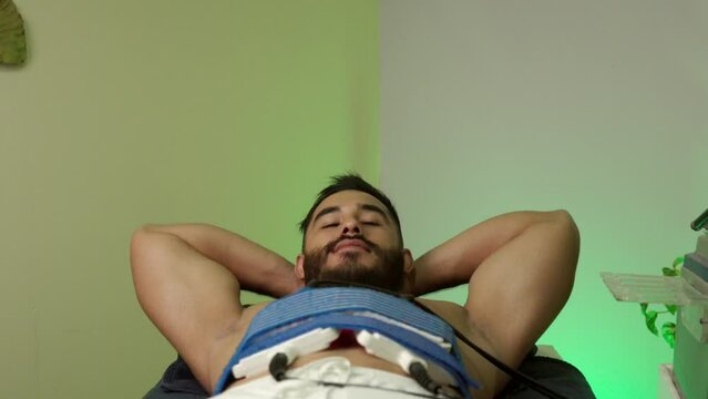 latin mexican male model muscle handsome guy smile while receive lipo laser treatment procedure at hotel spa wellness center fat loss