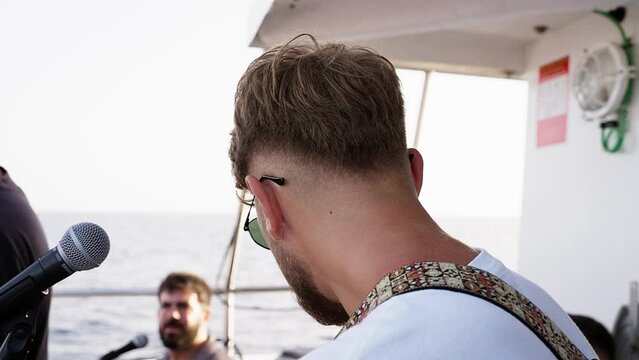 Group of diverse friend singing on deck of yacht while yachting together. Attractive young men hanging out, celebrating holiday vacation trip while catamaran boat sailing during summer sunset.