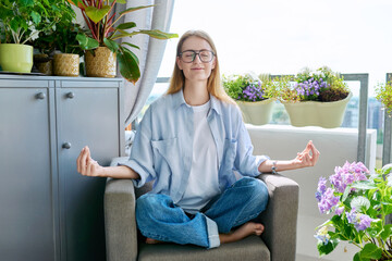 Young teenage girl relaxing meditating at home with her eyes closed in lotus position