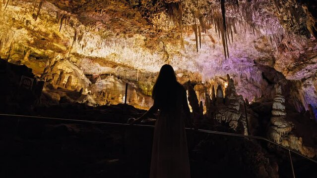 A tourist girl exploring underground cave tunnels of rocky formations in Majorca. A colourful natural scenery in a cave with ancient cavities formed of carbonate limestone rocks in Mallorca, Spain.