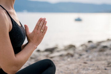 Meditation on sea beach. Young woman practicing hatha yoga. Girl relaxing on coast. Concept of mental health, calmness, mindfulness, female wellbeing. Retreat in nature outdoors. Close up of hands