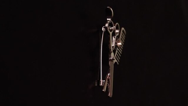A brooch for a hairdresser. A brooch in the form of scissors and a comb. On a black background. Rotates on an electric turntable display stand. Vertical video.