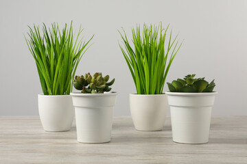 Many different artificial plants in flower pots on wooden table against light grey background