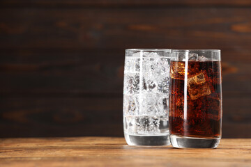 Glasses of different refreshing soda water with ice cubes on wooden table, space for text