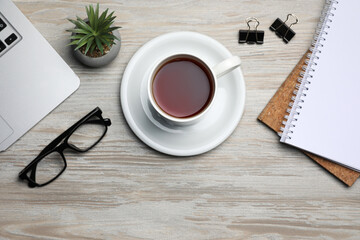 Obraz na płótnie Canvas Ceramic mug of aromatic tea, laptop, glasses, houseplant and notebooks on white wooden table, flat lay