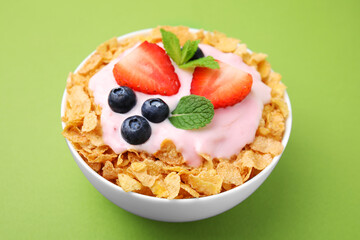 Delicious crispy cornflakes, yogurt and fresh berries in bowl on green background, closeup. Healthy breakfast