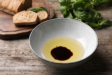 Bowl of balsamic vinegar with oil and bread on old wooden table, closeup