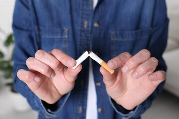 Woman breaking cigarette on blurred background, closeup. Stop smoking concept