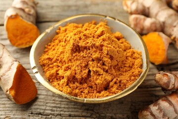 Aromatic turmeric powder and raw roots on wooden table, closeup