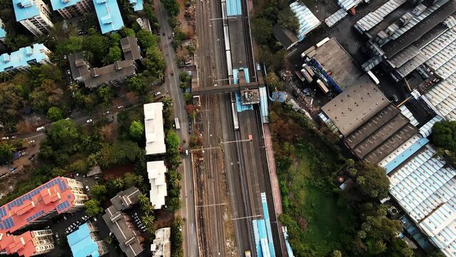 Aerial footage of rail locomotive moving from train station towards city. Drone shot of railway train moving to Mumbai City. Urban train aerial video. Indian commuter train in city. Urban commuter