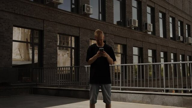 A man in a black T-shirt and shorts looks at the smartphone screen.