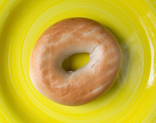 Single plain bagel on a yellow plate top view - 641663752