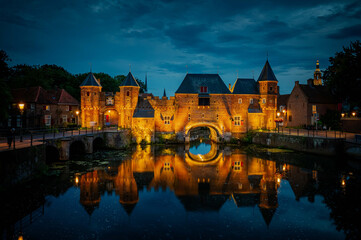 Medieval fortress city wall gate Koppelpoort and Eem River in the city of Amersfoort by night,...