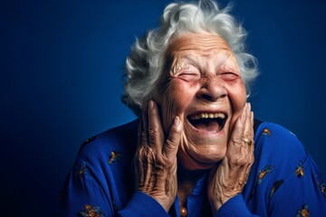 Close-up portrait photography of a joyful old woman placing the hand over the mouth in a laughter gesture against a royal blue background. With generative AI technology