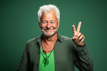 Headshot portrait photography of a joyful mature man making a peace gesture with two fingers against a green background. With generative AI technology