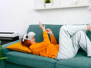 woman laying on sofa relaxing and playing VR and using futuristic artificial intelligence at home.. the concept of metaverse, virtual reality, future, technology, and internet of things.