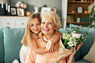 Cheerful little girl giving flowers to grandmother indoors - obrazy, fototapety, plakaty
