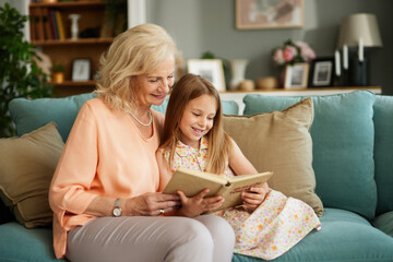 Grandma and granddaughter reading a book at home