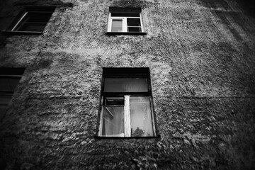 The black-white photo depicts an old, grey, and somber building with dark windows. Sadness and nostalgia, decay. The emptiness of the building may also suggest themes of abandonment, loss and neglect.