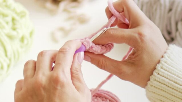 Women's hands knit with crochet hook and woolen fluffy pink threads. Handmade yarn hobby and craft.	