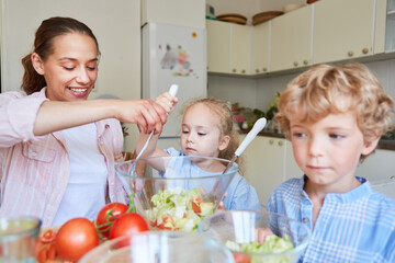 Obraz na płótnie Canvas Mother preparing salad with children in kitchen