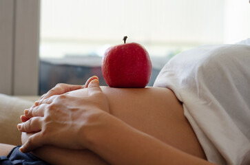 Pregnant woman with an apple on her belly. Concept of healthy lifestyle and balanced nutrition during pregnancy and maternity.