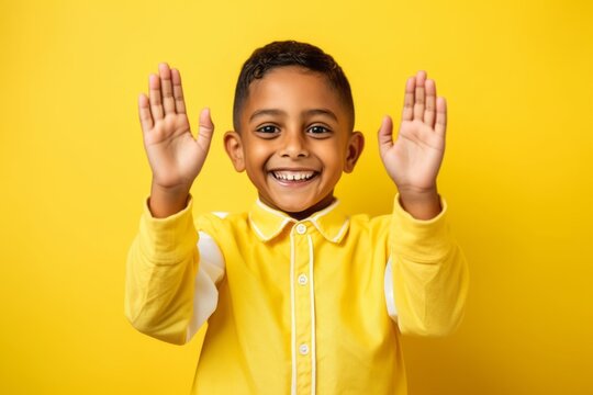 Lifestyle portrait photography of a grinning kid male joining palms in a gesture of gratitude against a bright yellow background. With generative AI technology