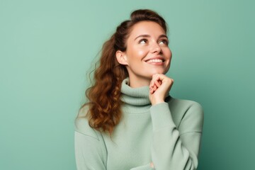 Medium shot portrait photography of a glad girl in her 20s putting the hand on the chin as if thinking against a pastel green background. With generative AI technology