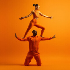 Fototapeta na wymiar Couple of gymnasts, dancers in their performance in sports equipment. leggings and a tracksuit on an orange background, hall.