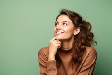 Lifestyle portrait photography of a satisfied girl in her 20s putting the hand on the chin as if thinking against a pastel green background. With generative AI technology