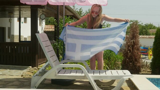 Girl in swimming costume lays out towel on sun lounger by swimming pool to sunbathe