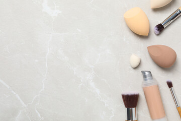 Cosmetic sponges, foundation and brushes on beige background, space for text