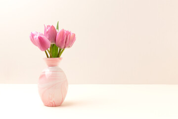 Vase with bouquet of pink tulip flowers in front of gray background. Copy space.