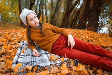 a young teenage girl is lying in a glade in the autumn forest, enjoying the beautiful nature and bright yellow leaves