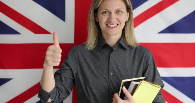 Young woman gives thumb up for language learning. Smiling English teacher standing in front of British flag and encouraging students to study