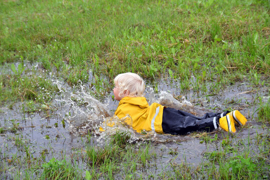 Little boy playing outdoor  in a muddy puddle on a rainy fall day