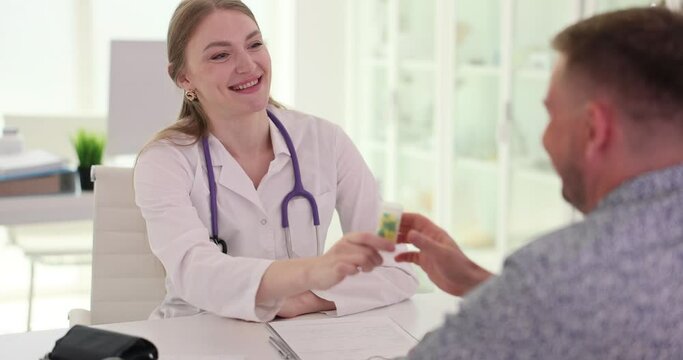 Woman general practitioner giving medicine in plastic bottle to male patient. Family doctor writing prescription for sick patient slow motion