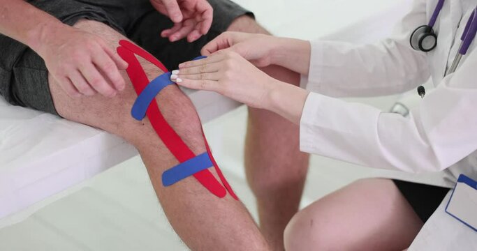 Practitioner applying kinesiology stretch tape to patient knee joint. Swelling and pain subsided of male. Trauma doctor at hospital slow motion