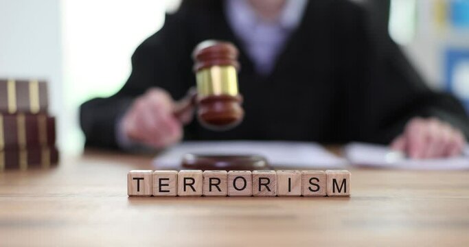 Word Terrorism made of wooden cubes against judge hitting gavel on sound block. Concept of criminality and reprimand from professional slow motion