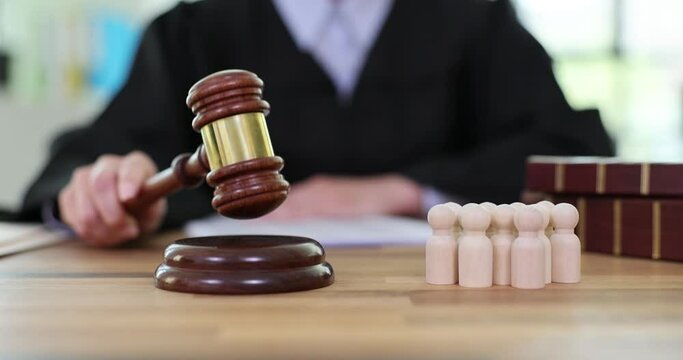 Judge in work uniform knocks gavel on sound block on table with wooden figurines in court office. Guilty and accomplices in commission of crime slow motion