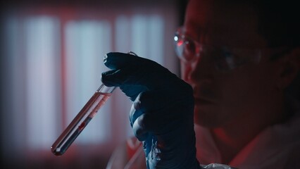 The forensic examiner examines a blood sample in a test tube with a reagent. A man in protective...