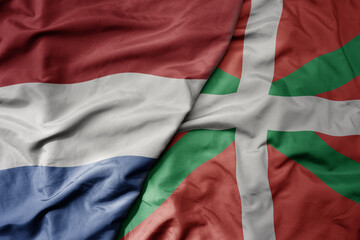 big waving national colorful flag of netherlands and national flag of basque country .
