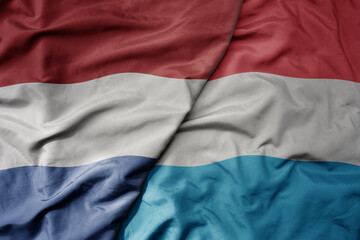 big waving national colorful flag of netherlands and national flag of luxembourg .