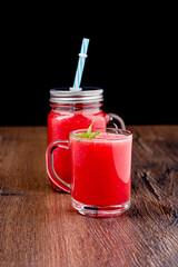 Watermelon smoothie with mint leaves in a glass mug and a glass jar with a lid.