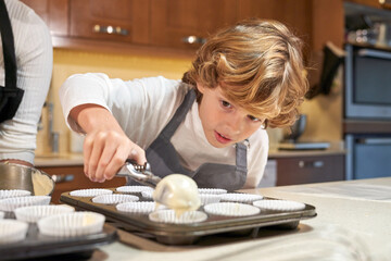 Cute boy filling cupcake baking tray