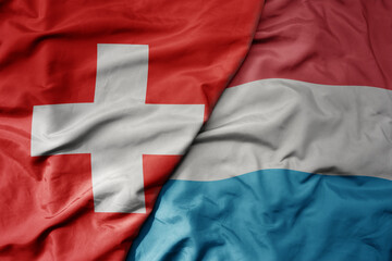 big waving national colorful flag of switzerland and national flag of luxembourg .